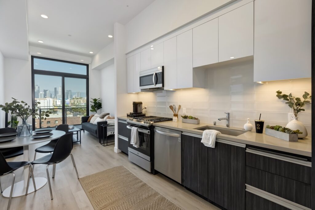 kitchen view with white and black cabinets, under cabinet lighting, stainless steel appliances, and view of the living area