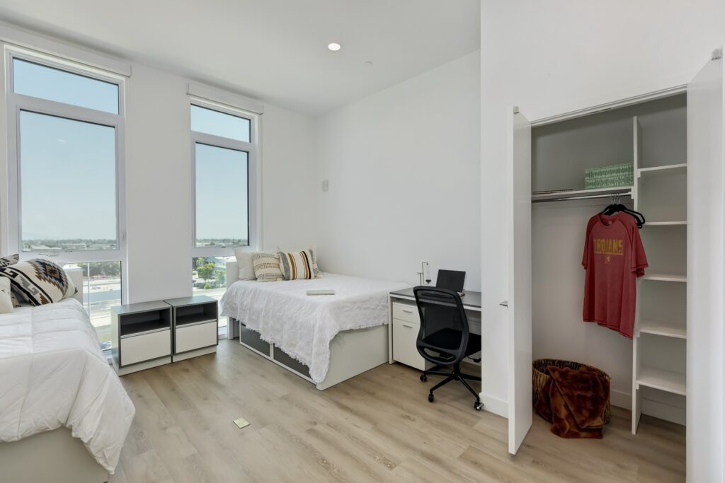 bedroom with two beds, small desk, two large windows, and closet with shelving
