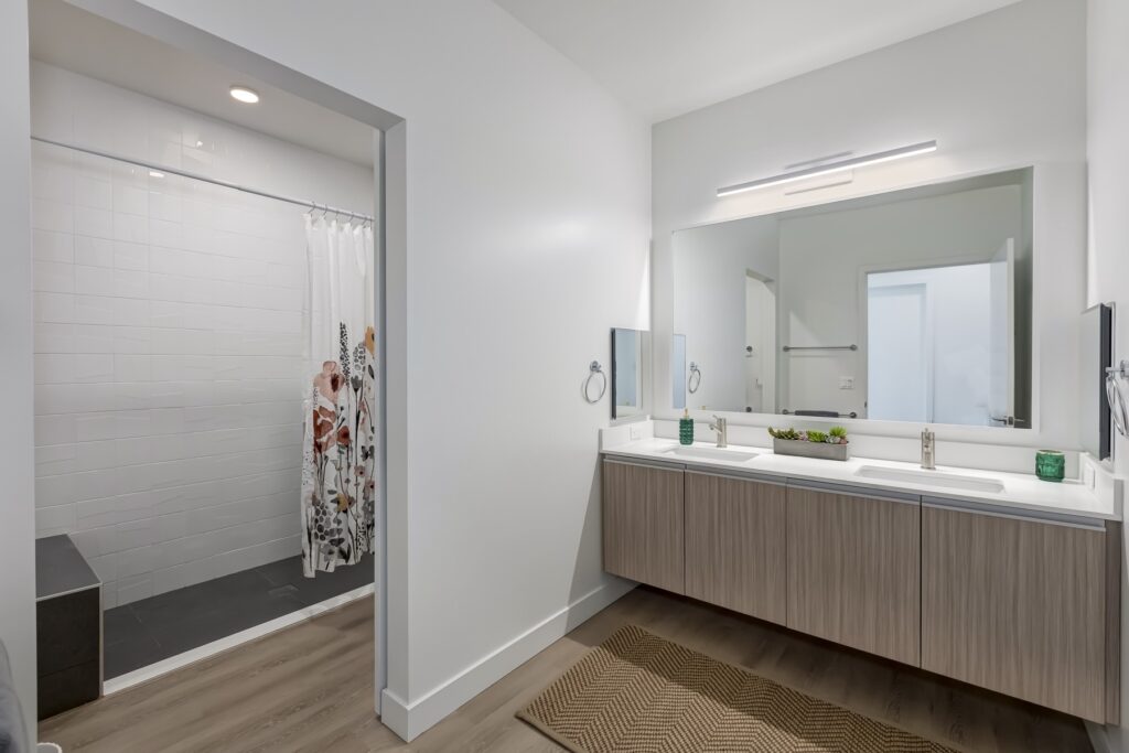 bathroom view with large main mirror, dual side mirrors, dual sinks, and walk-in shower with bench