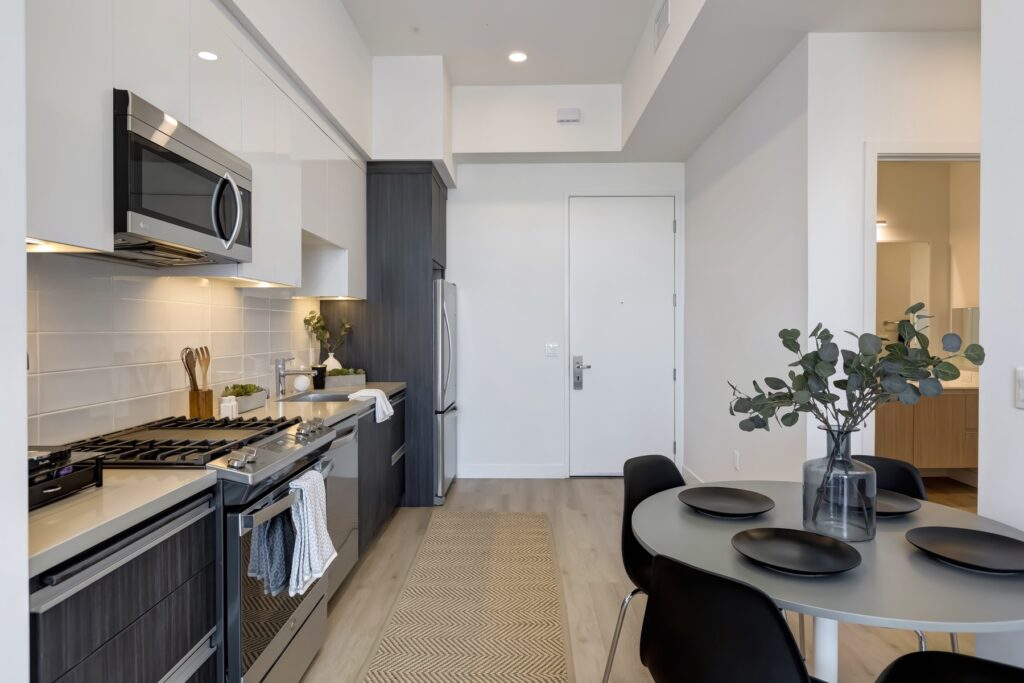 kitchen view with white and black cabinets, stainless steel appliances, under cabinet lighting, view of the front door, and dining table