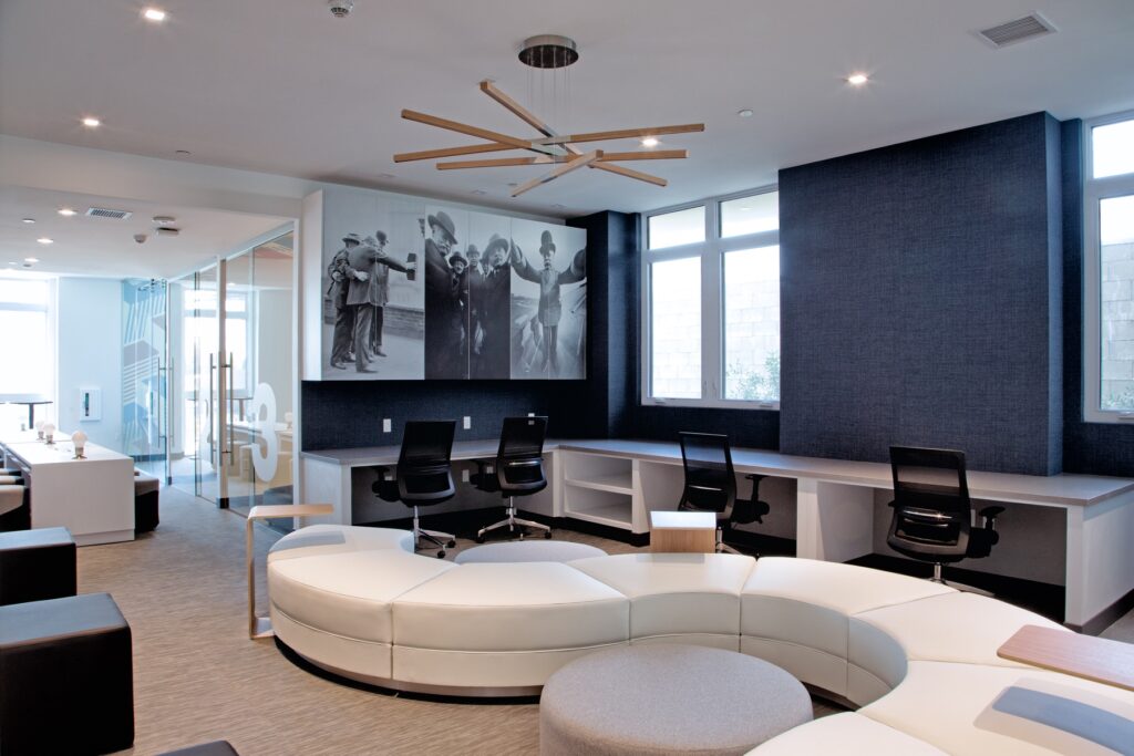 Interior clubhouse with lounge and table seating, computer desks, designer lighting, windows, and carpet flooring