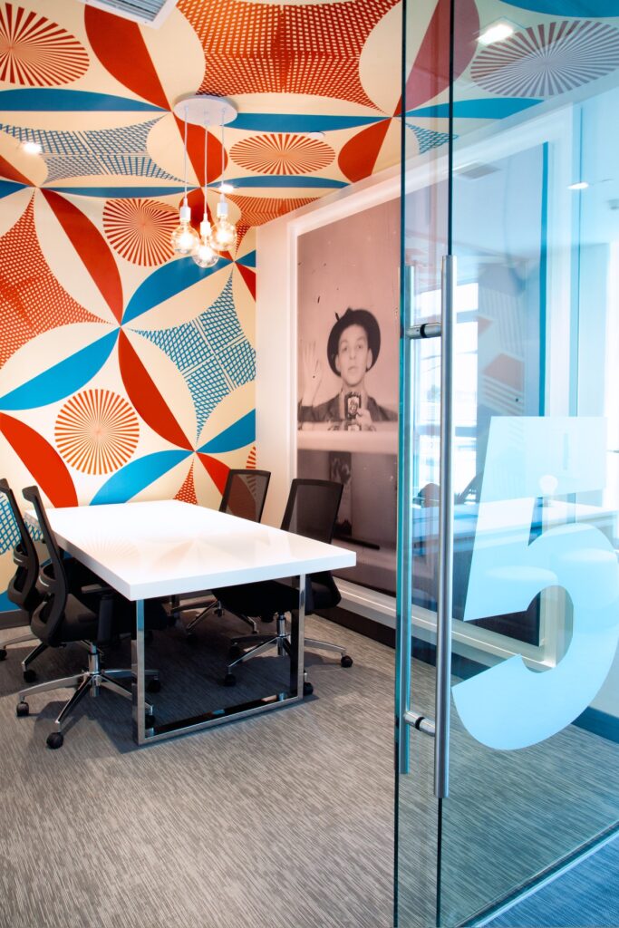 Clubhouse meeting room with chair seating, desk table, accent colored walls, carpet flooring, and designer lighting