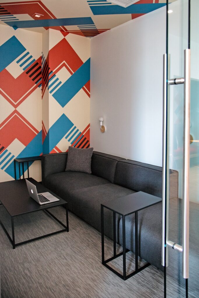 Clubhouse meeting room with couch seating, coffee table, a laptop, accent colored walls, carpet flooring, and designer lighting