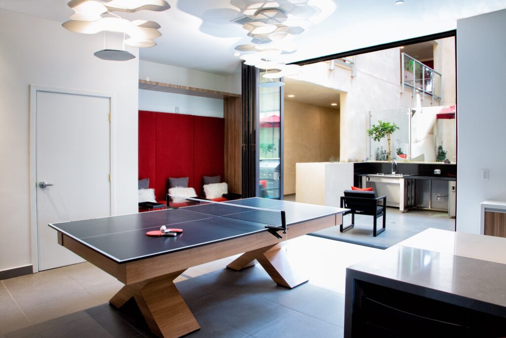 Interior clubhouse lounge with ping pong table, open access to outdoor courtyard, lounge seating, tile flooring, and outdoor and designer lighting