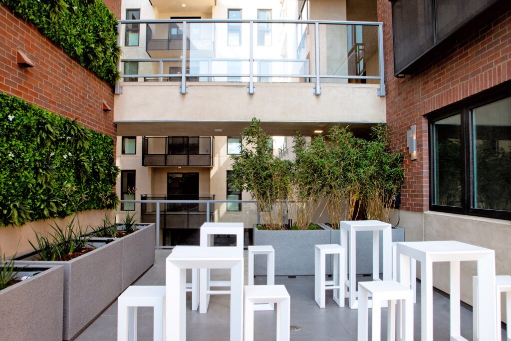 Outdoor courtyard with surrounding plants and gardens, overlooking balcony, and designer table seating