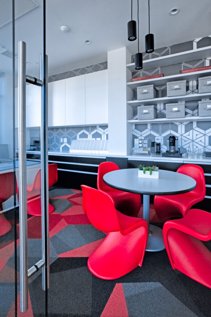 Interior clubhouse kitchen and bar area with carpet flooring, table seating, and coffee makers