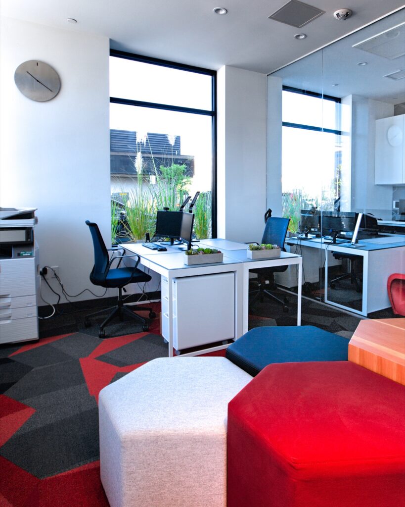 Interior clubhouse computer lab with computer desks, computers and monitors, printer, large windows, carpet flooring, and lounge seating