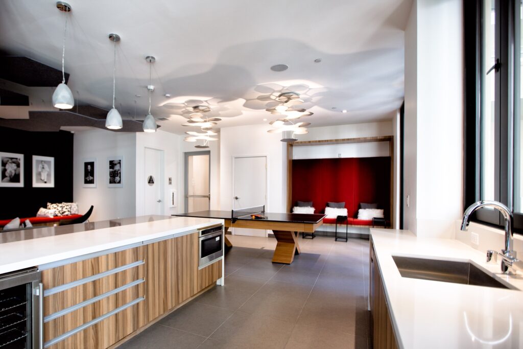 Interior clubhouse lounge area with ping pong table, sink, lounge seating, designer lighting, and tile flooring