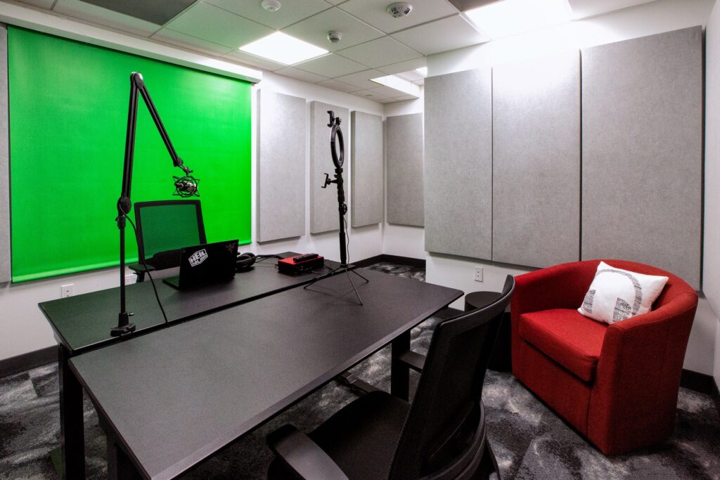 Indoor clubhouse DJ room with microphones, lighting, green screen, desk seating, lounging chairs, and carpet flooring