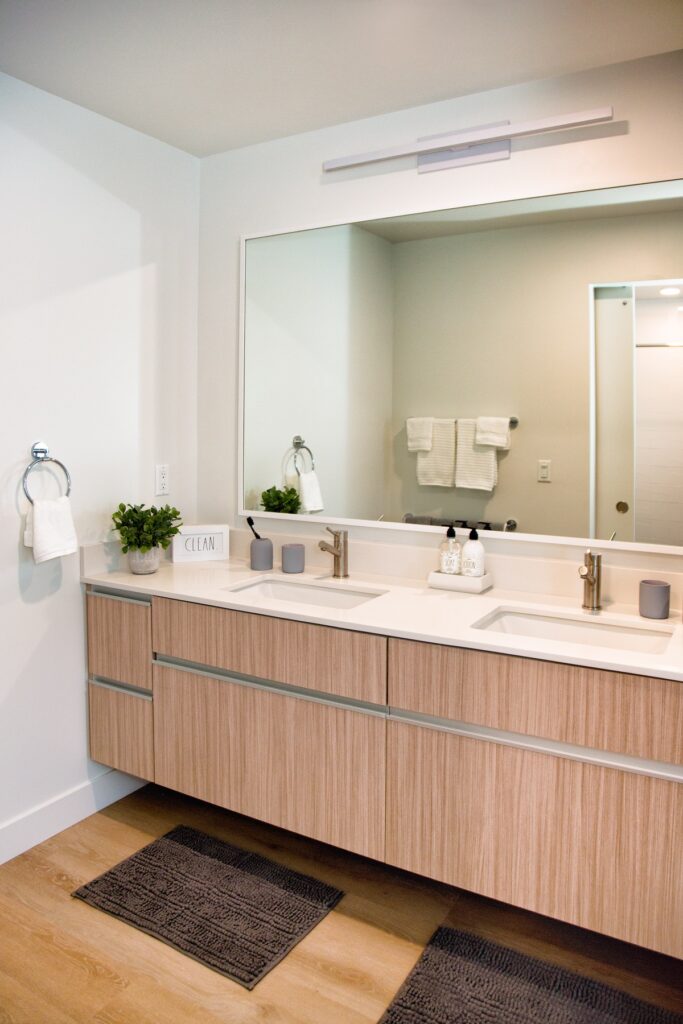 Bathroom area with dual sinks, large mirror, wood-style flooring, and designer lighting