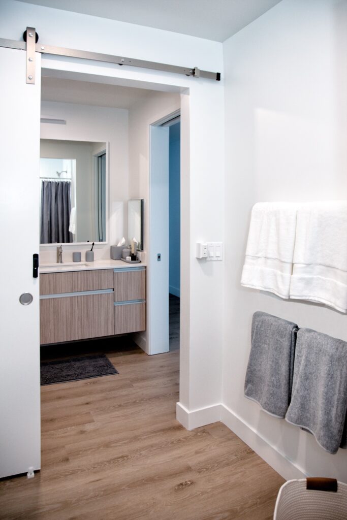 Bathroom area with dual sinks, large mirror, towels, wood-style flooring, and designer lighting