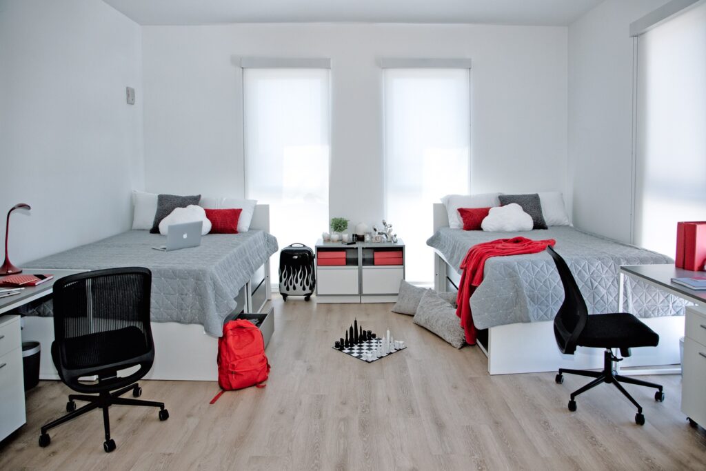 Bedroom area with two twin beds, computer desks, floor-to-ceiling windows, and wood-style flooring