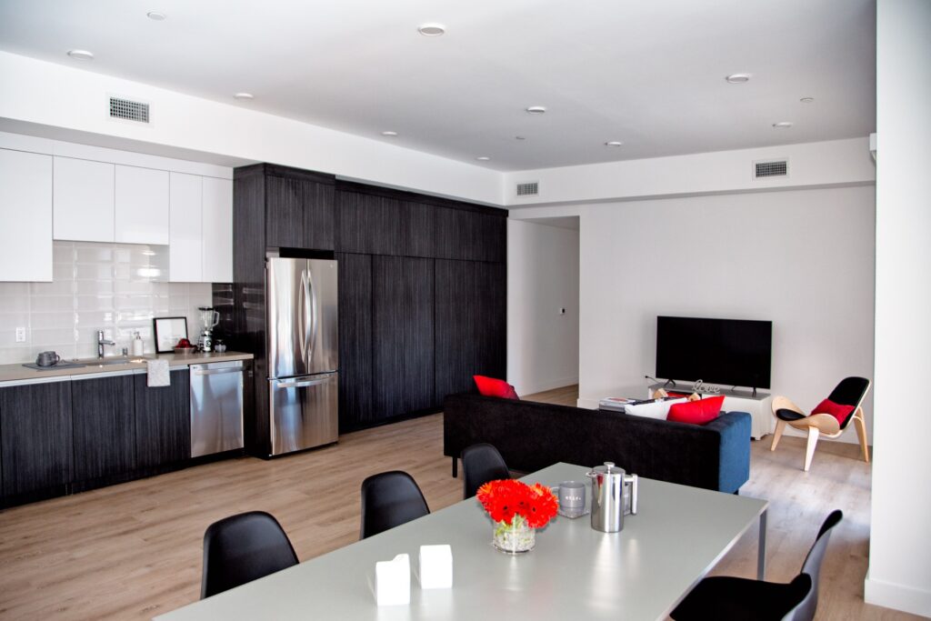 Living room and kitchen area with couch, television, dining table, stainless steel appliances, and wood-style flooring